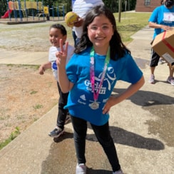 GOTR girls poses outside at her school with a medal around her neck after completing the 5K